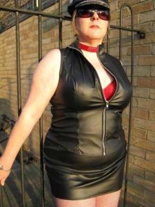 Vivian in black vinyl dress and leather cap, with red fishnet stockings.
